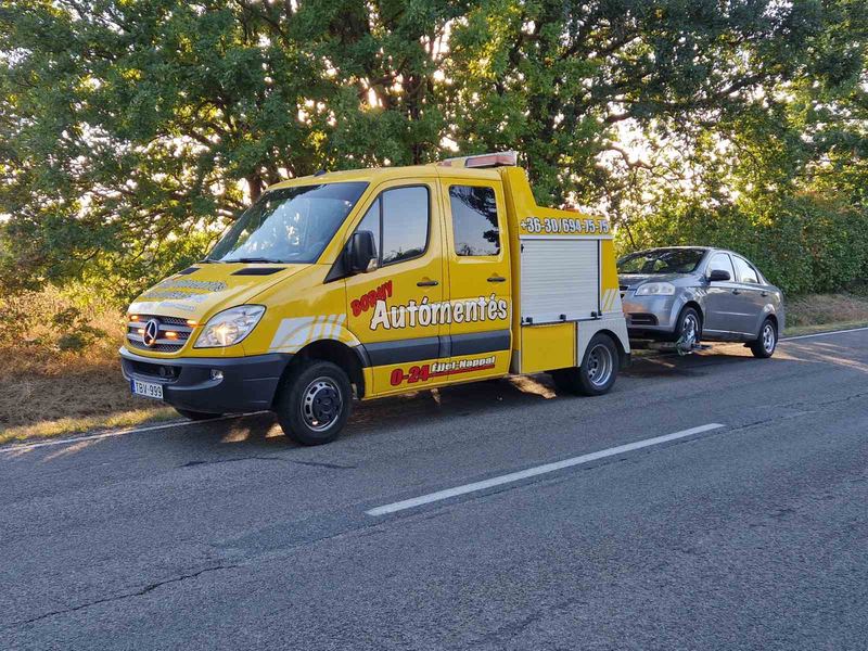 Mercedes Sprinter emelővontató személyautót vontat naplementében